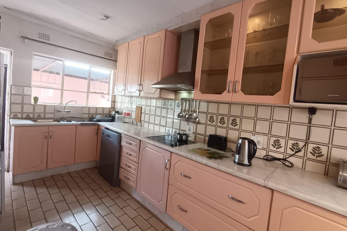 A functional kitchen featuring dated pastel cabinetry, ceramic tile backsplash, stainless steel extractor fan, and tiled flooring.