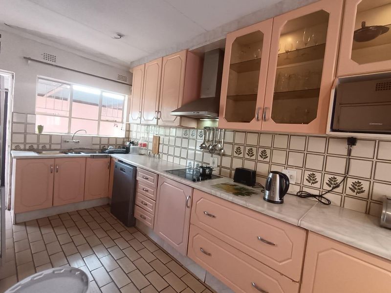 A functional kitchen featuring dated pastel cabinetry, ceramic tile backsplash, stainless steel extractor fan, and tiled flooring.