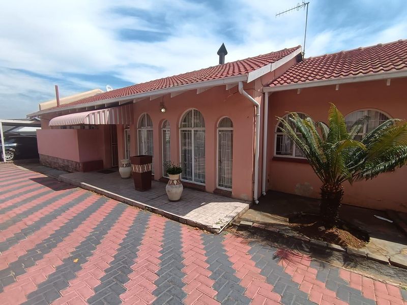 Front elevation of a single-story house featuring a tiled roof, arched windows, and a paved driveway with an attached awning.