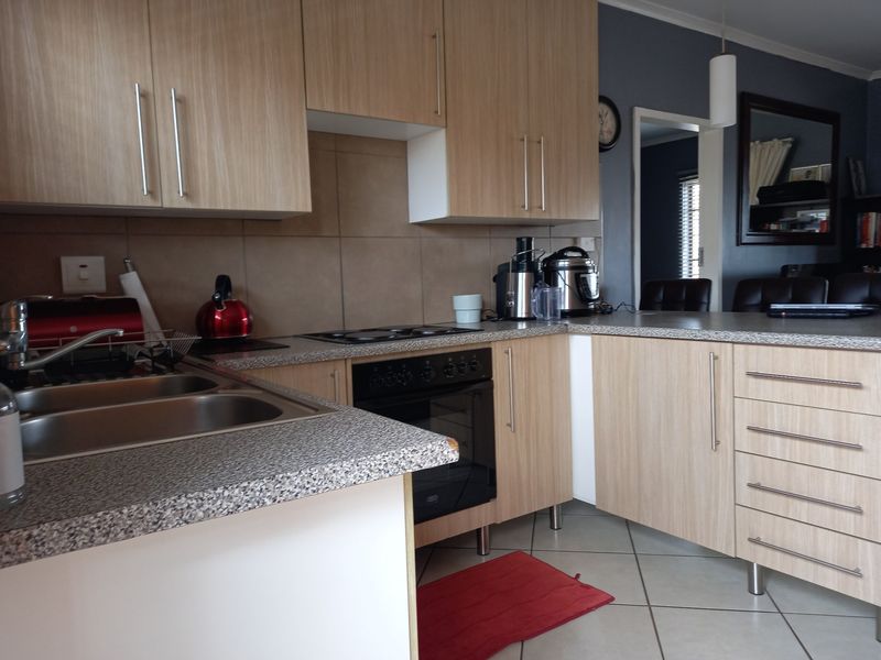 Functional kitchen featuring light wood-look cabinetry, laminate countertops, built-in oven, electric hob, and tiled flooring with a neutral backsplash.