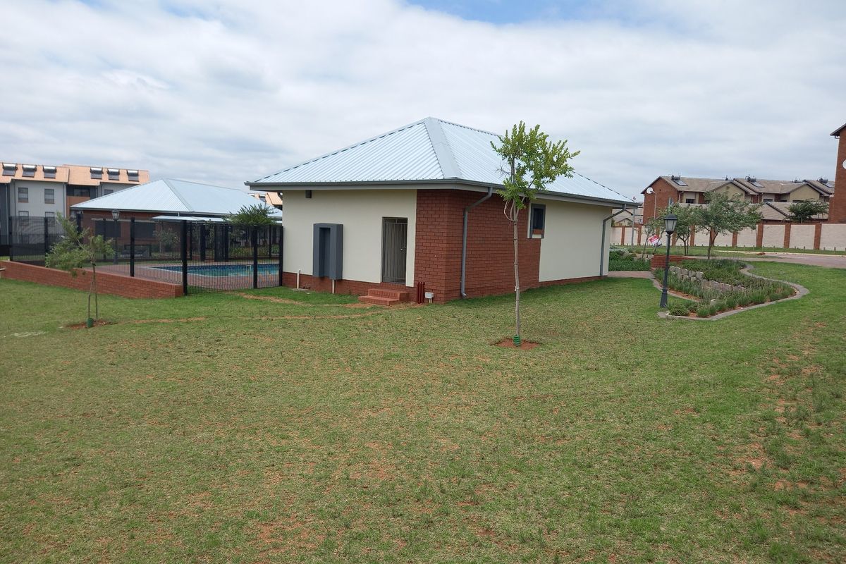 Exterior view of a residential building featuring a metal roof, brick facade, and access to a communal swimming pool and landscaped garden area.