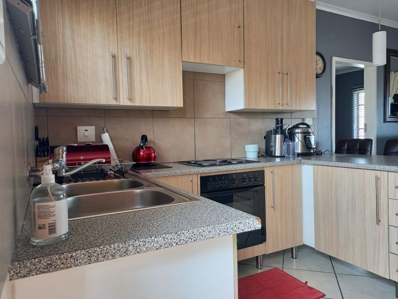 Functional kitchen featuring light wood-finish cabinetry, laminate countertops, a built-in oven with electric hob, and tiled backsplash.