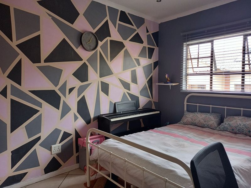 A bedroom featuring tiled flooring, venetian blinds, and a decorative geometric painted accent wall.