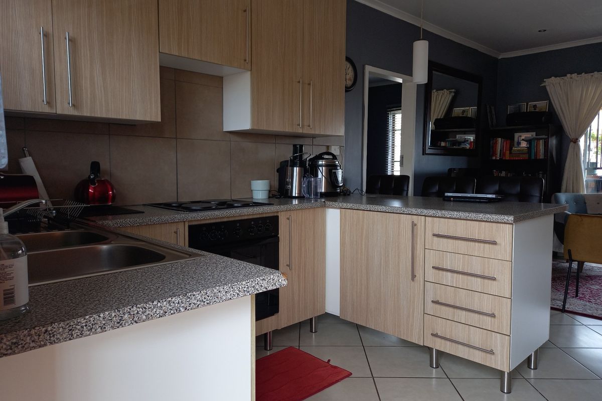 A functional kitchen featuring light wood-grain cabinetry, granite-look countertops, a built-in oven with hob, and tiled flooring, seamlessly flowing into the adjacent living area.