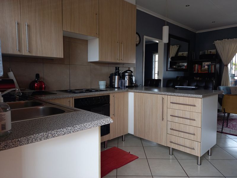 A functional kitchen featuring light wood-grain cabinetry, granite-look countertops, a built-in oven with hob, and tiled flooring, seamlessly flowing into the adjacent living area.