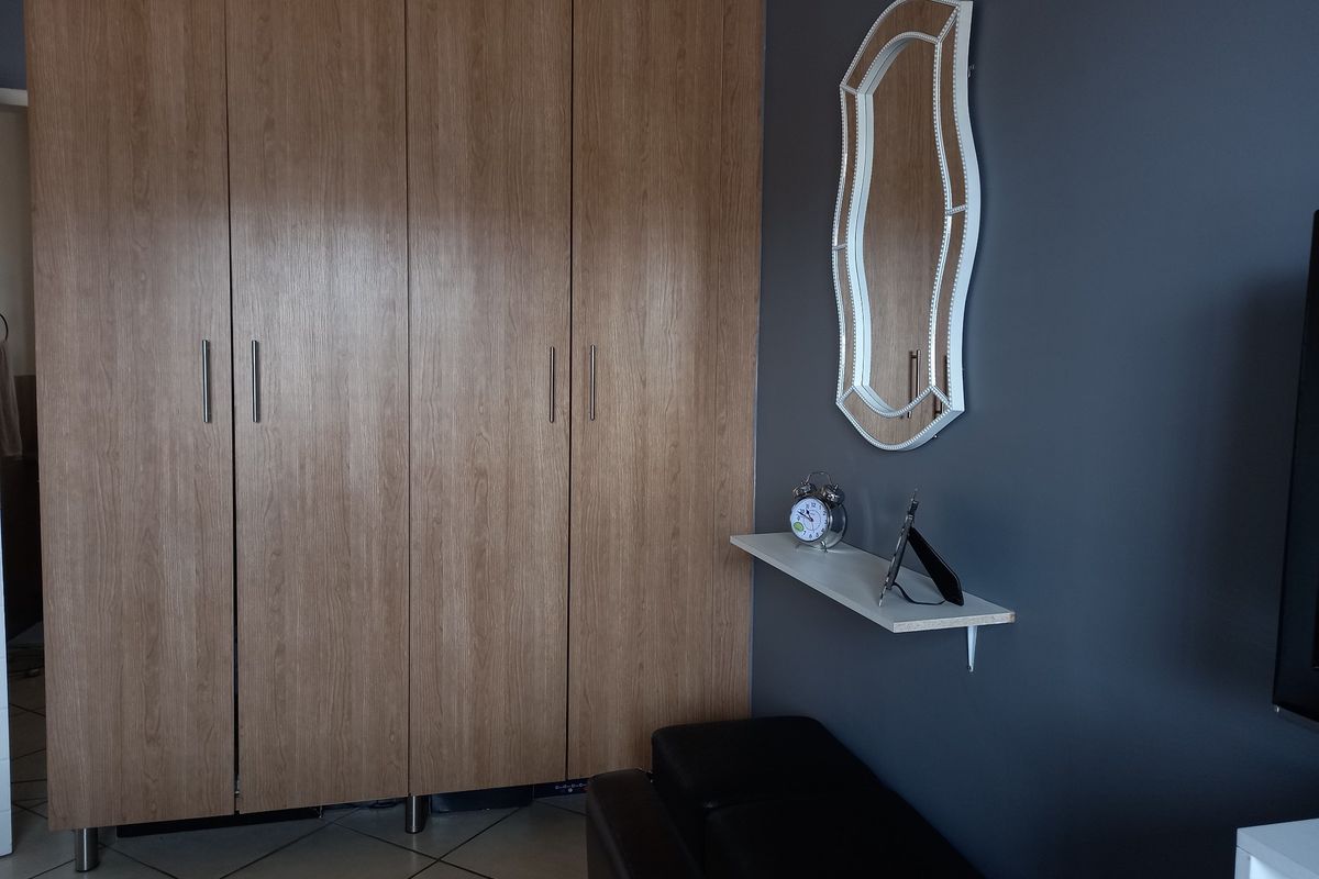 A bedroom featuring light wood-finish built-in wardrobes, dark grey accent wall, and tiled flooring.