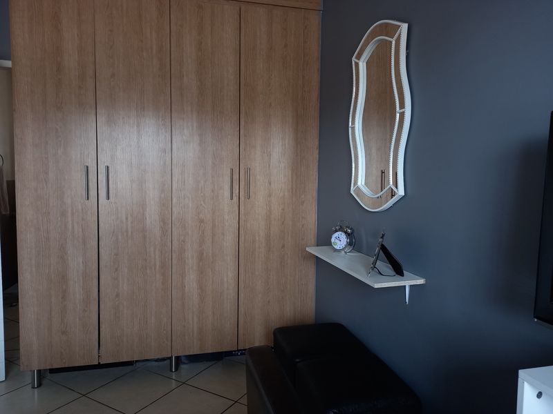 A bedroom featuring light wood-finish built-in wardrobes, dark grey accent wall, and tiled flooring.