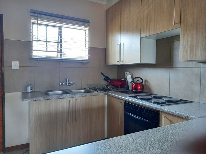 A functional kitchen featuring laminate cabinetry, granite-look countertops, a double bowl sink, and built-in electric cooking appliances with tiled splashbacks.