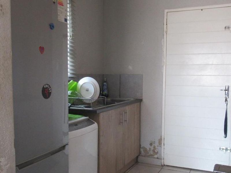 A compact scullery area featuring built-in cabinetry, a sink, and tiled flooring, currently showing signs of wall damage requiring maintenance.