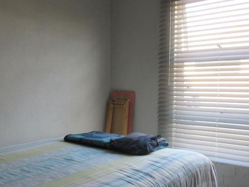 A simple bedroom featuring a window with fitted venetian blinds, providing natural light and basic privacy.