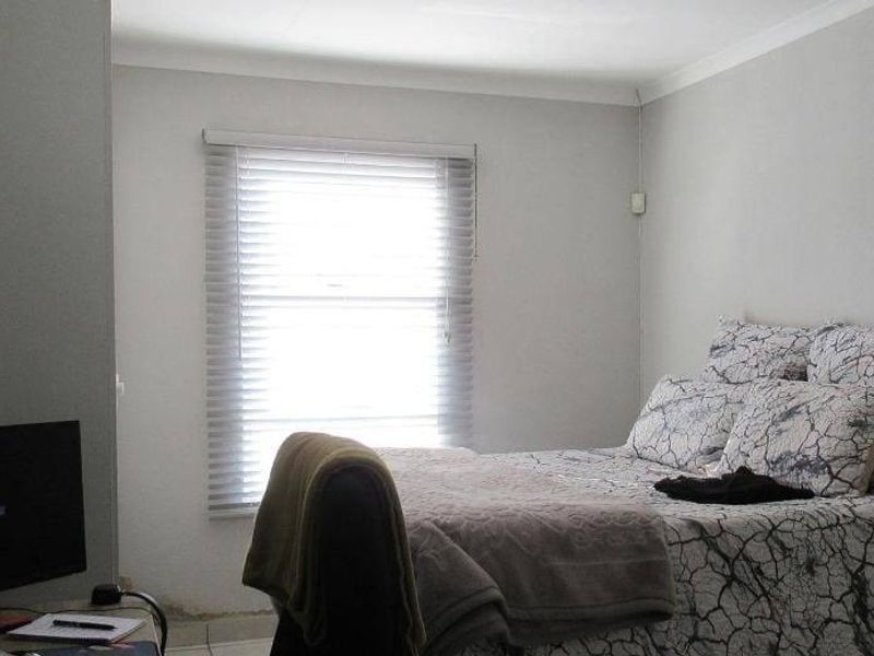 A bedroom featuring neutral walls, built-in storage, and venetian blinds, showing signs of moisture damage near the base of the wall.
