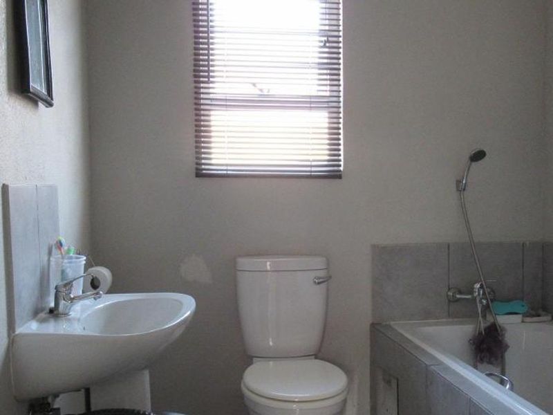 A functional bathroom featuring a pedestal basin, toilet, and a bathtub with a handheld shower mixer, finished with neutral wall tones.