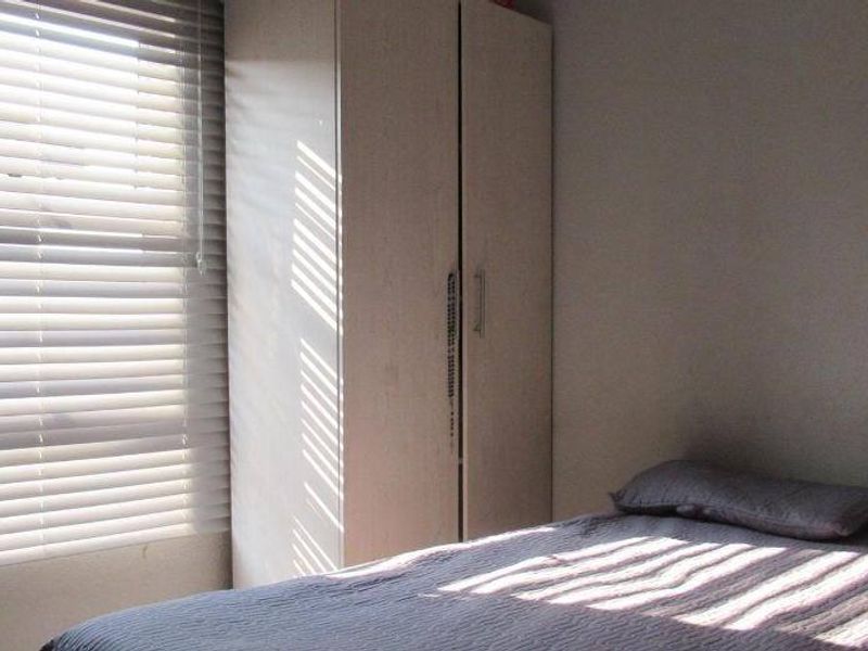 A functional bedroom featuring a built-in wardrobe and venetian blinds, providing natural light and storage space.