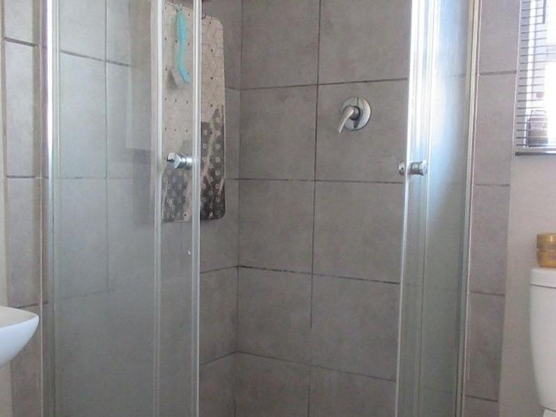 A functional bathroom featuring a glass shower enclosure, wall-mounted basin, and toilet with neutral grey wall tiling.