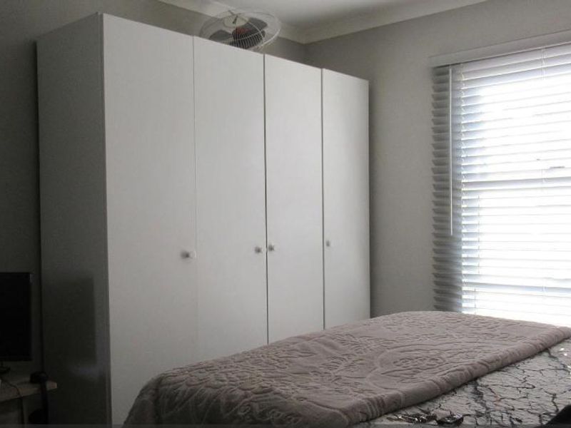 A bedroom featuring a large white built-in wardrobe, venetian blinds, and a ceiling fan.