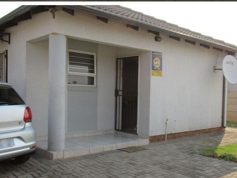 Front exterior view of a single-story house featuring a paved driveway, covered entrance porch with a concrete column, and a secure boundary wall.