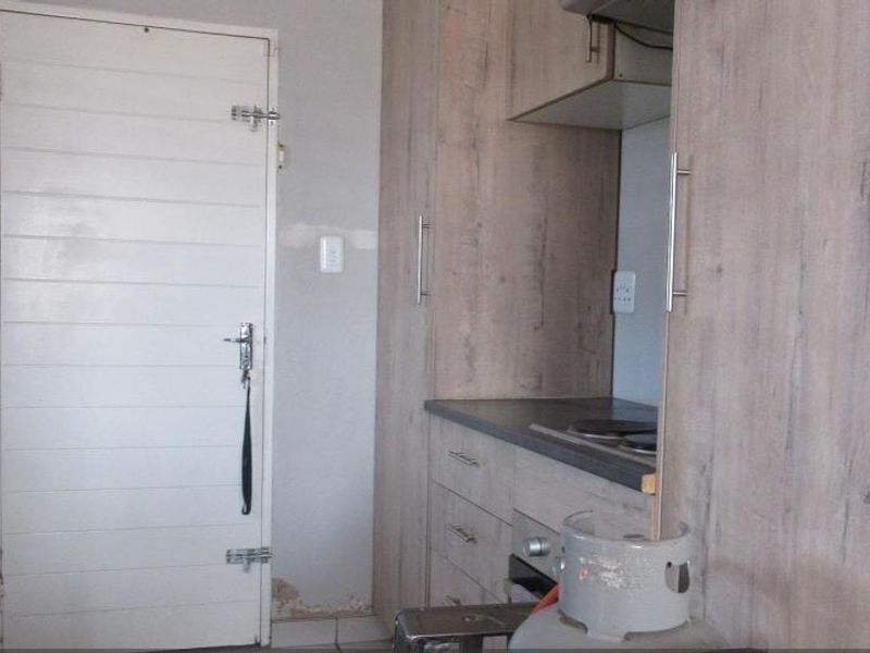 A compact kitchen featuring wood-look cabinetry, built-in oven and hob, and tiled flooring. The walls show signs of moisture damage requiring repair.