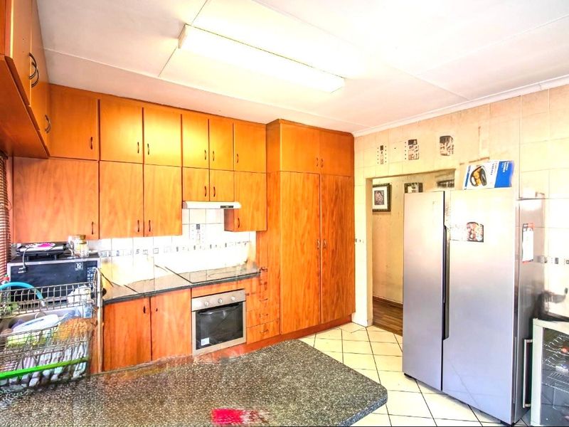 A functional kitchen featuring extensive wooden cabinetry, granite countertops, built-in oven, and tiled finishes, offering a classic layout with ample storage space.