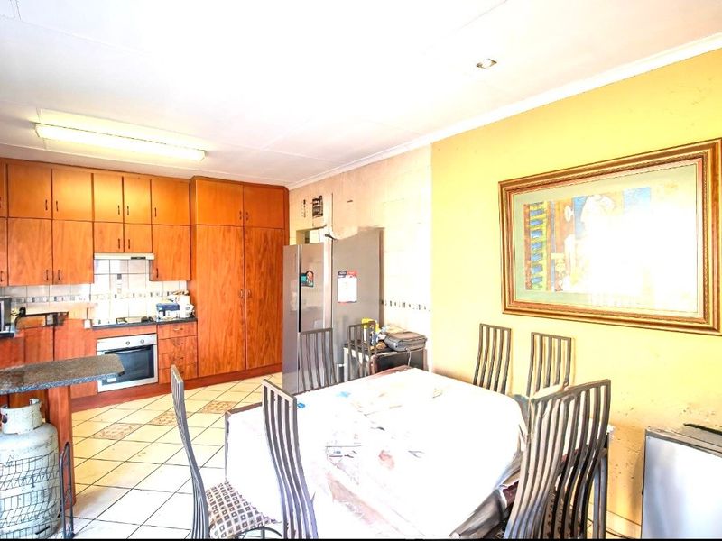 Open-plan kitchen and dining area featuring wooden cabinetry, built-in oven, and tiled flooring, offering a functional space in need of cosmetic updates.