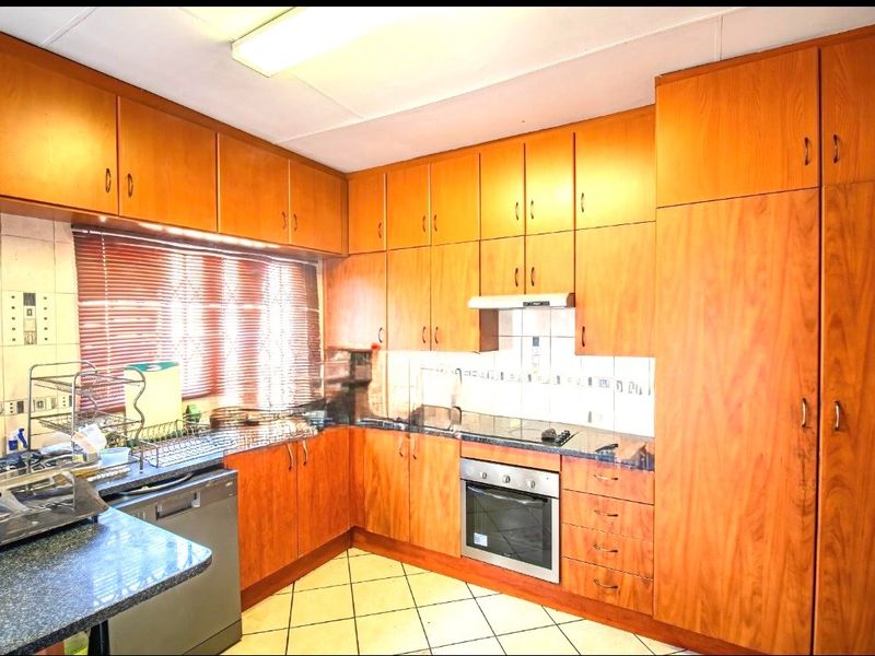 A functional kitchen featuring extensive built-in wooden cabinetry, laminate countertops, a built-in oven with hob, and tiled flooring.