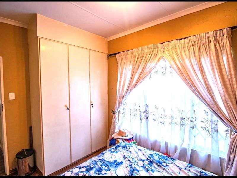 A bedroom featuring built-in cupboards and a window with curtains, offering a functional space with potential for cosmetic updates.