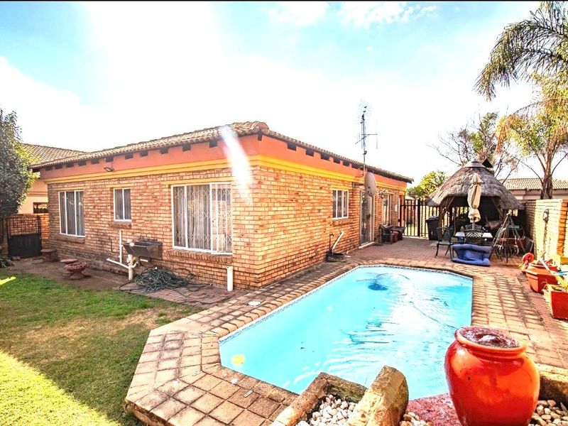 Rear exterior view featuring a swimming pool, brick paved patio area, and a traditional thatched lapa in a private garden setting.