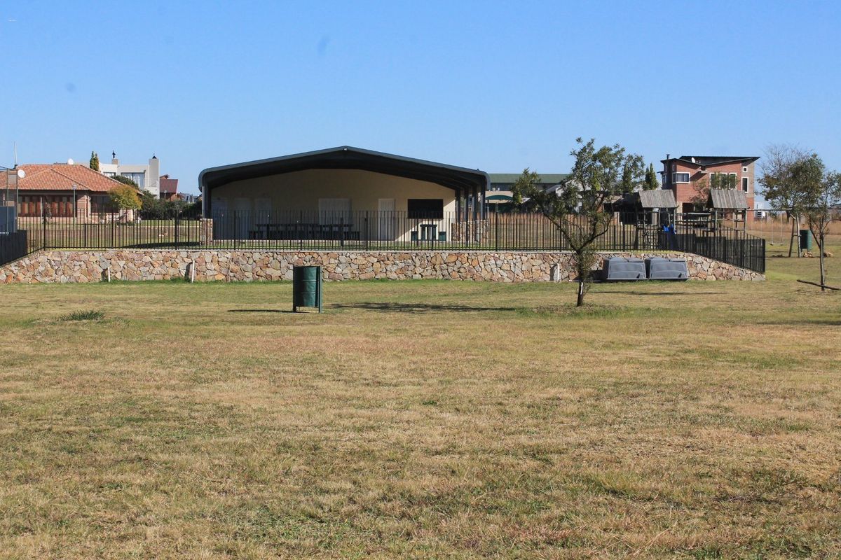 A view of a residential property featuring a stone retaining wall, metal fencing, and a covered outdoor pavilion set within a spacious lawn area.