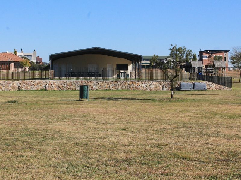 A view of a residential property featuring a stone retaining wall, metal fencing, and a covered outdoor pavilion set within a spacious lawn area.