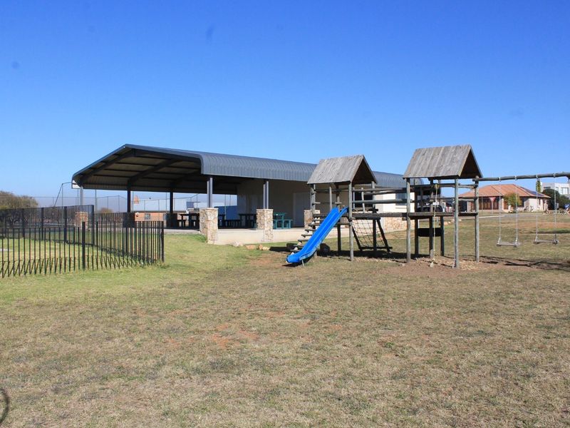 Outdoor communal area featuring a covered patio structure, stone pillars, and a playground set situated on a grassy lot.