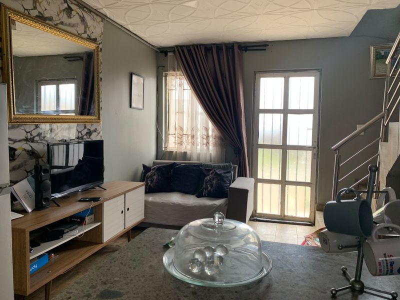 A living room area featuring a staircase with a metal balustrade, tiled flooring, and a glass panel door leading to the exterior.