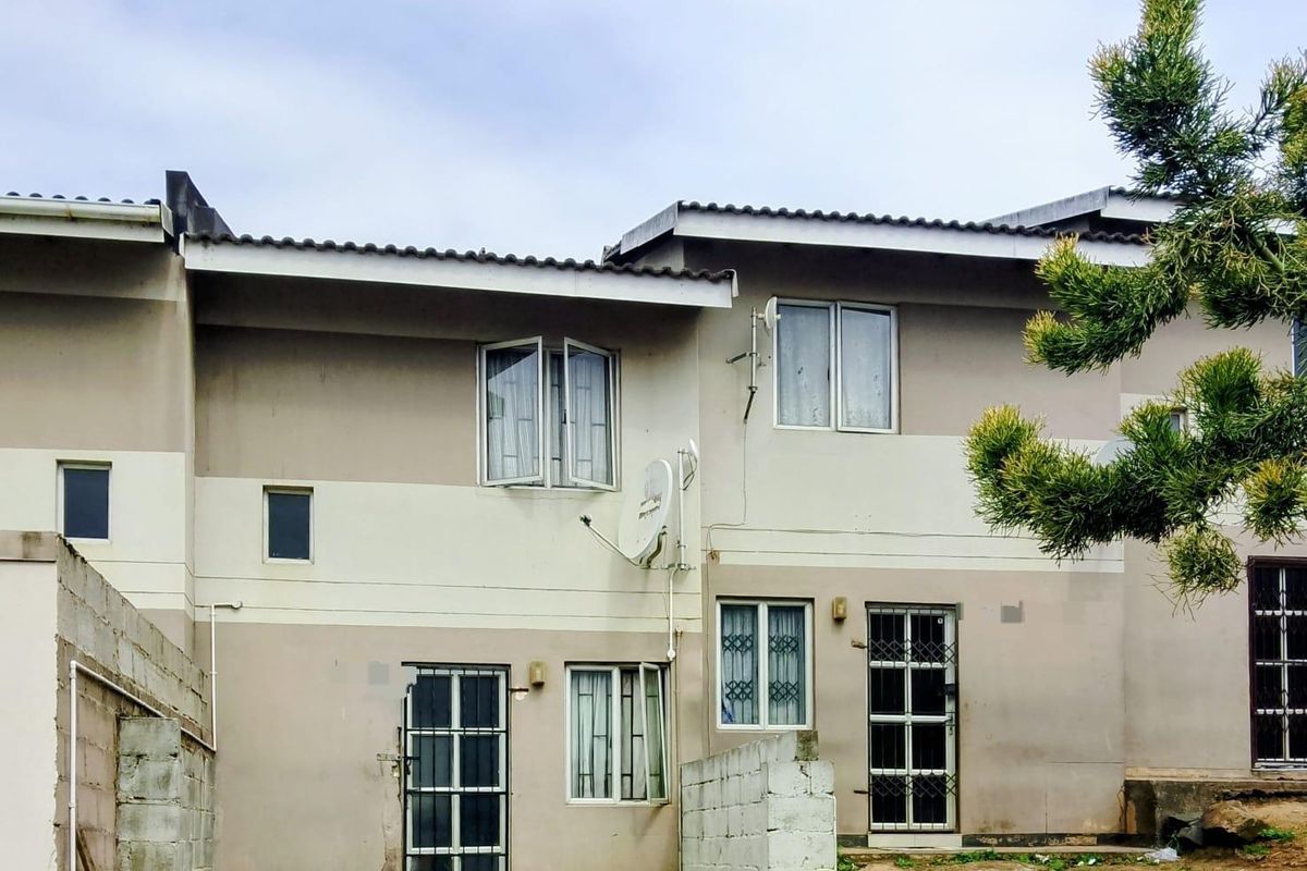 Rear elevation of a multi-story townhouse featuring security gates, aluminium windows, and an unfinished concrete boundary wall in the backyard area.