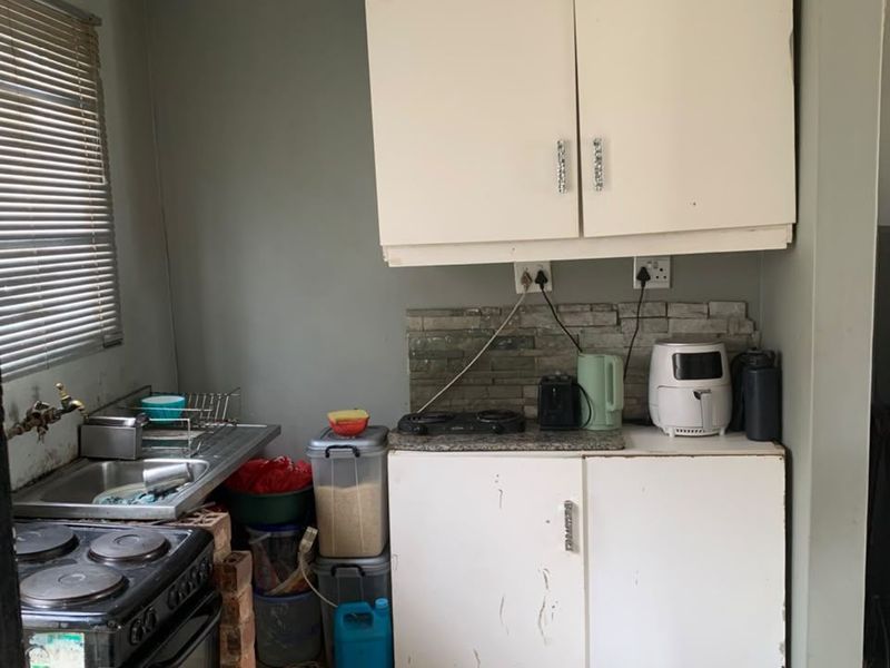 Compact kitchen area featuring built-in cabinetry, a stone-look splashback, stainless steel sink, and tiled flooring, requiring cosmetic updates to improve functionality and aesthetic appeal.
