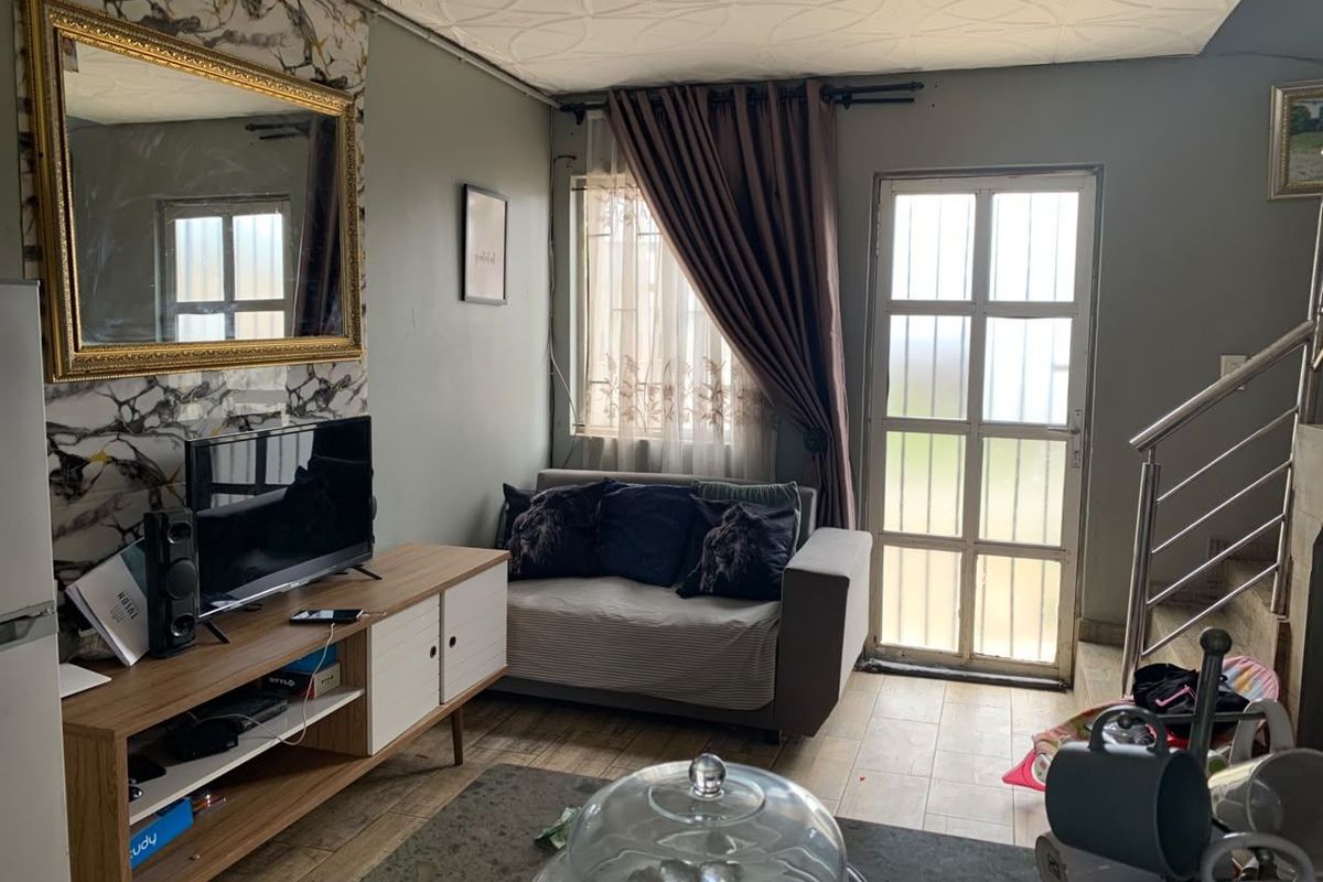 A compact living area featuring tiled flooring, a glass-panelled exterior door, and a staircase with a metal railing.
