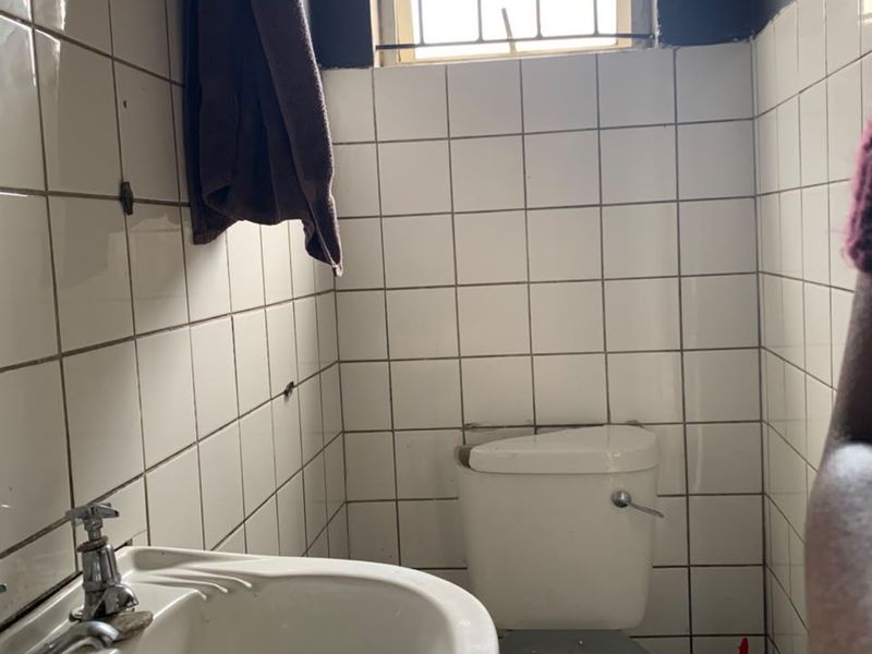 A small bathroom featuring a pedestal washbasin, flush toilet, and white wall tiling. The space requires renovation and updated fixtures.