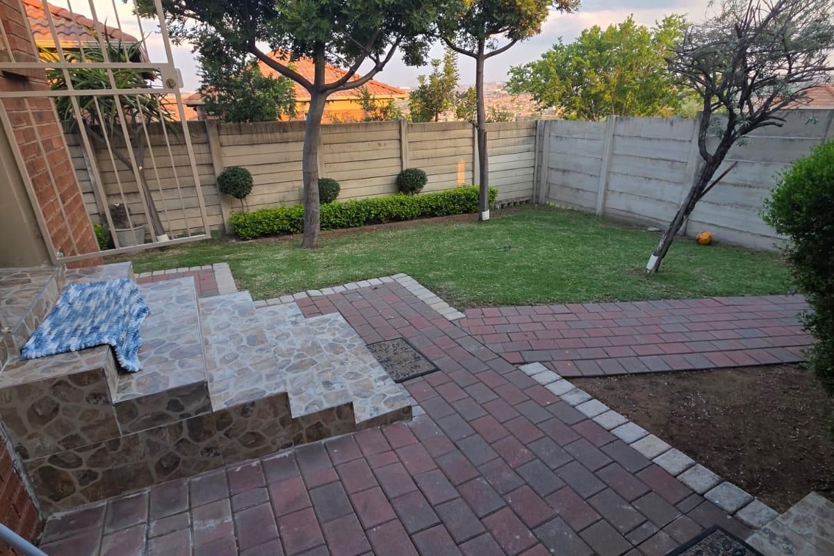 A well-maintained rear garden featuring a paved patio area, tiled steps, and a secure precast concrete boundary wall.