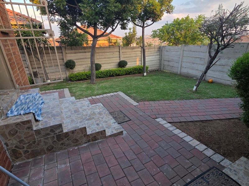A well-maintained rear garden featuring a paved patio area, tiled steps, and a secure precast concrete boundary wall.