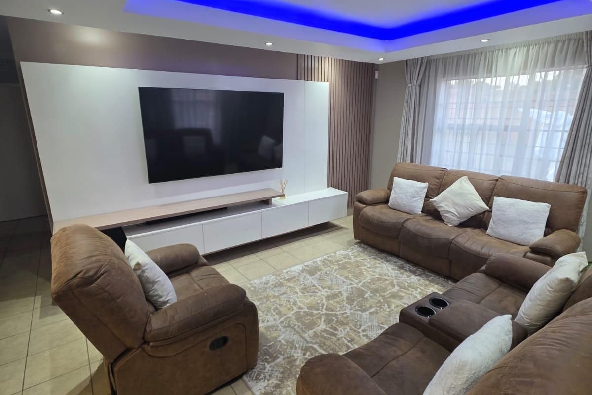 A modern living room featuring a built-in media wall, recessed ceiling with ambient LED lighting, and tiled flooring.