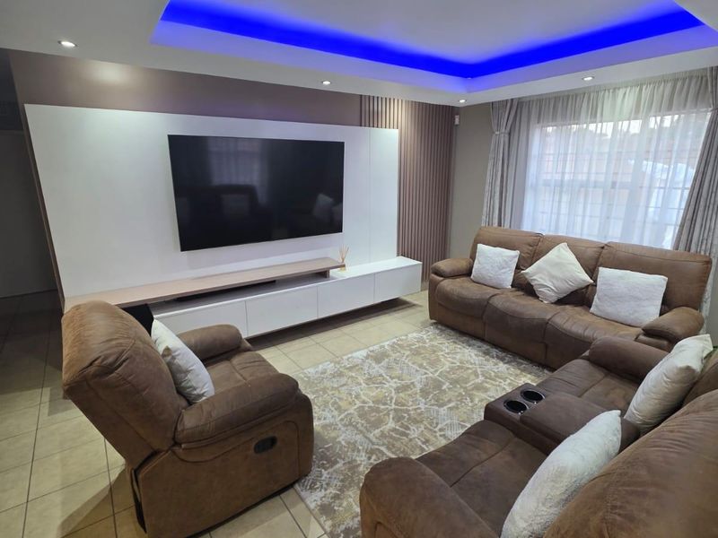 A modern living room featuring a built-in media wall, recessed ceiling with ambient LED lighting, and tiled flooring.