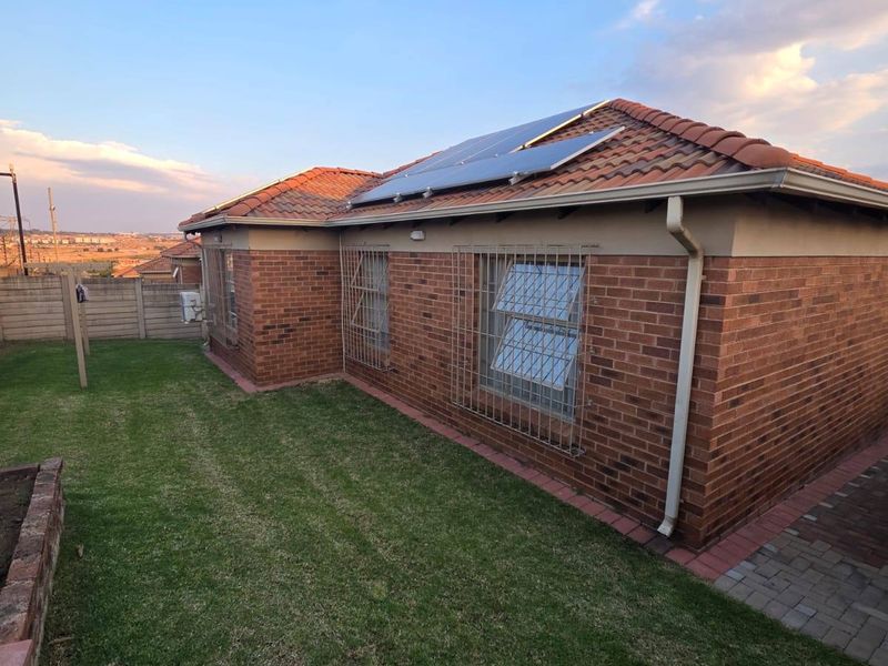 Rear view of a brick house featuring a tiled roof with installed solar panels, security bars on windows, and a well-maintained lawn.