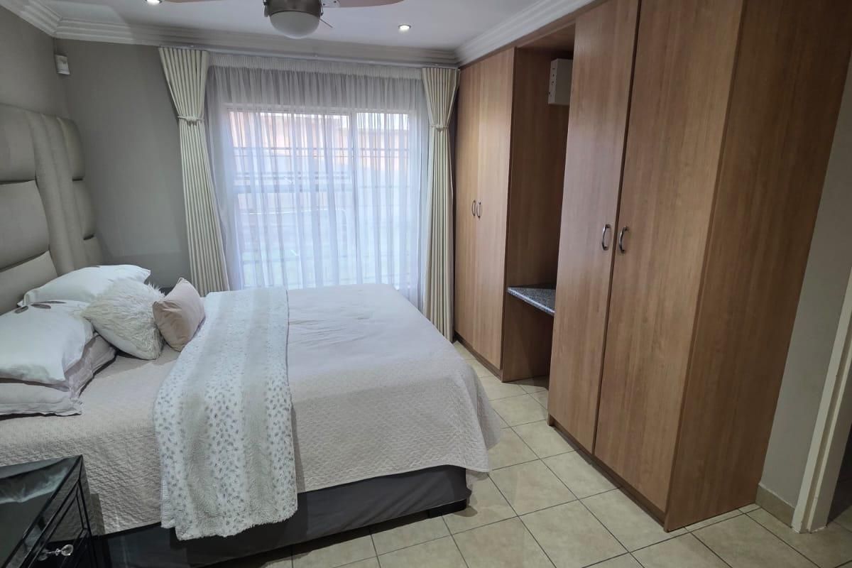 A well-maintained bedroom featuring built-in wooden cupboards, tiled flooring, and a ceiling fan, offering a clean and functional living space.