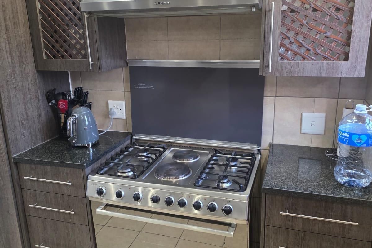 A well-maintained kitchen featuring dark wood cabinetry, granite countertops, a stainless steel gas and electric stove, and a tiled backsplash.