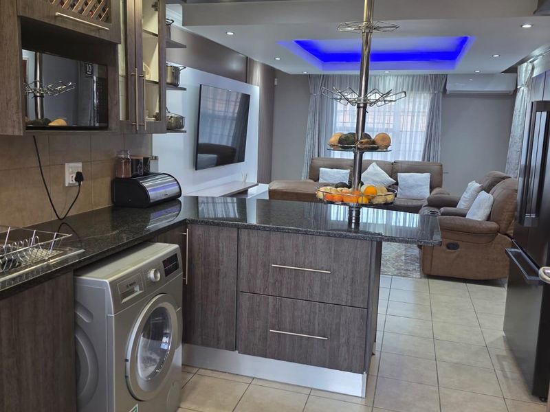 Modern open-plan kitchen and living area featuring dark wood cabinetry, granite countertops, recessed lighting, and tiled flooring throughout.