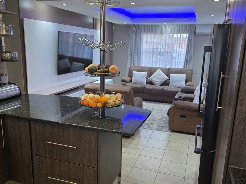 An open-plan living and kitchen area featuring dark wood cabinetry, granite countertops, tiled floors, and modern recessed ceiling lighting with blue accent features.