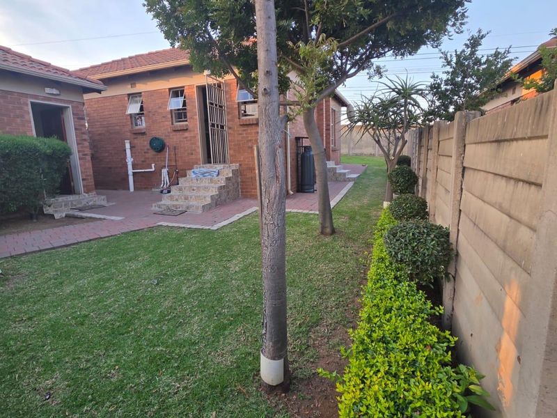 A well-maintained rear exterior view featuring a brick facade, paved patio area, and a landscaped garden enclosed by a precast concrete boundary wall.