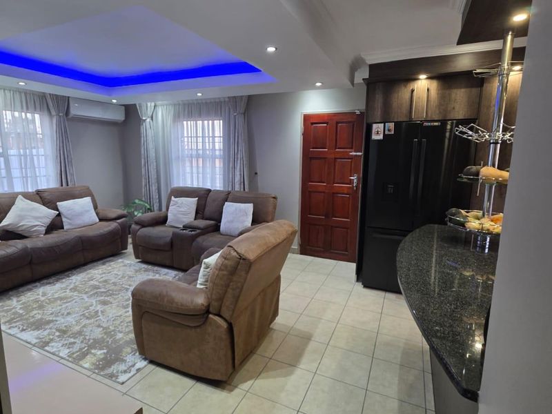 Open-plan living area featuring a modern kitchen with granite countertops, tiled flooring, and a recessed ceiling with integrated blue LED accent lighting.