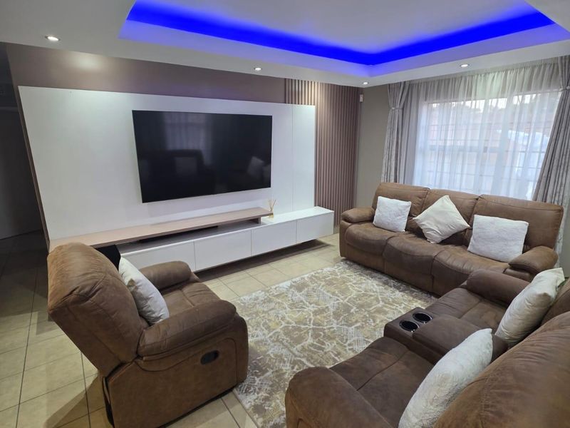 Modern living room featuring a custom media wall unit, recessed ceiling with ambient blue LED lighting, and neutral tiled flooring.