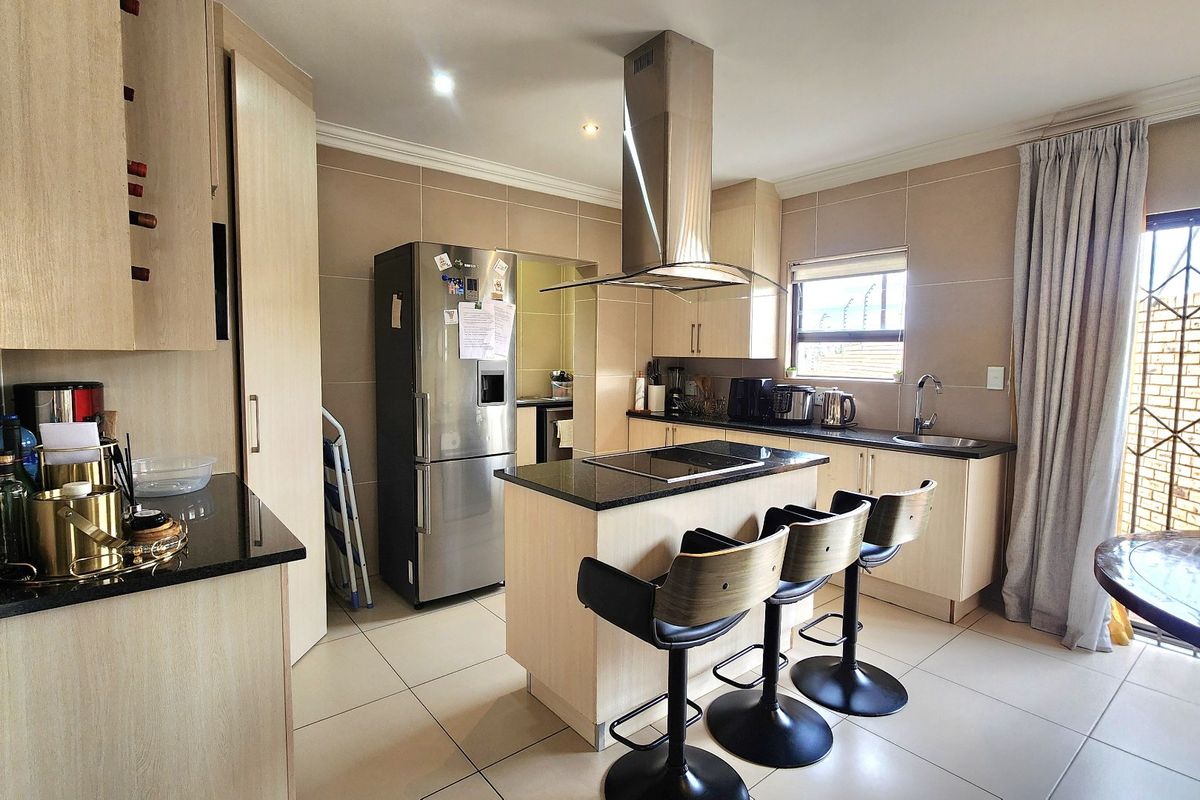 Modern kitchen featuring a central island with a built-in hob, granite countertops, ample cabinetry, and tiled flooring, offering a functional and well-maintained cooking space.