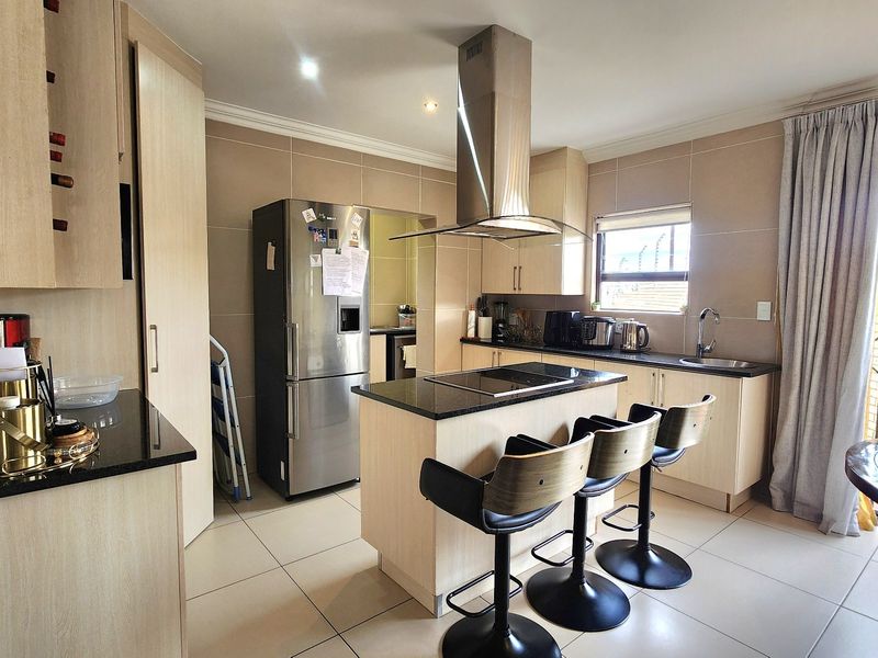 Modern kitchen featuring a central island with a built-in hob, granite countertops, ample cabinetry, and tiled flooring, offering a functional and well-maintained cooking space.