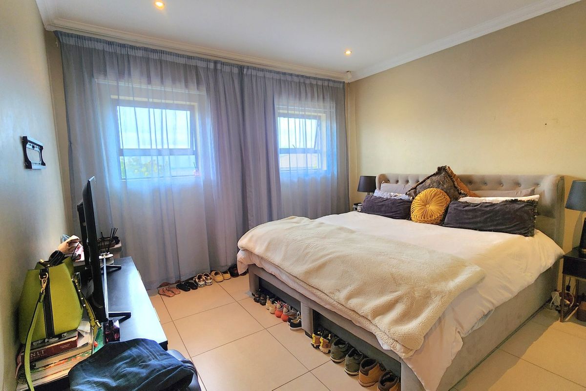 A well-lit bedroom featuring tiled flooring, recessed downlighting, and large windows with sheer curtains, providing a comfortable and functional living space.