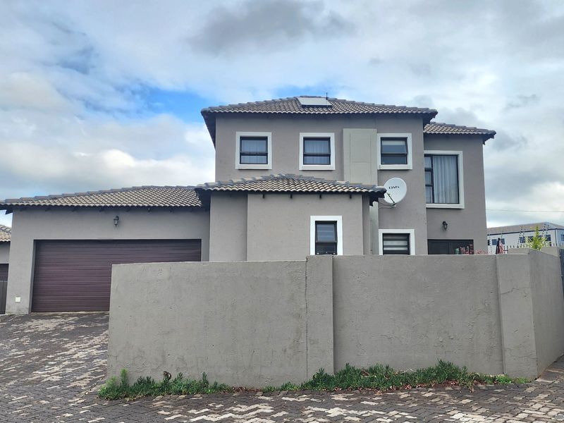 A modern double-storey cluster home featuring a paved driveway, double garage, and a secure boundary wall under a tiled roof.